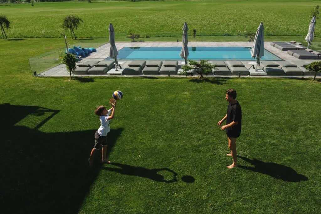 Mann und Junge spielen Volleyball auf einer Wiese am Pool
