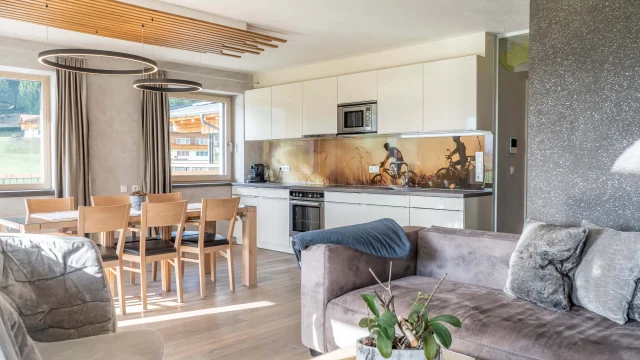 Moderner Wohnbereich mit offener Küche, Holzesstisch und grauem Sofa.