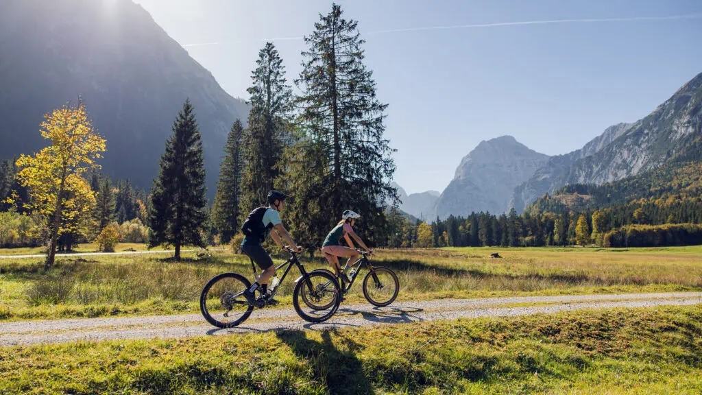 Zwei Mountainbiker auf einem sonnigen Schotterweg in den Alpen.