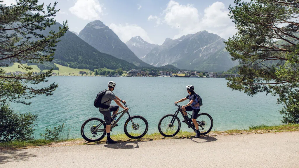 Zwei Mountainbiker blicken auf einen Bergsee in den Alpen.