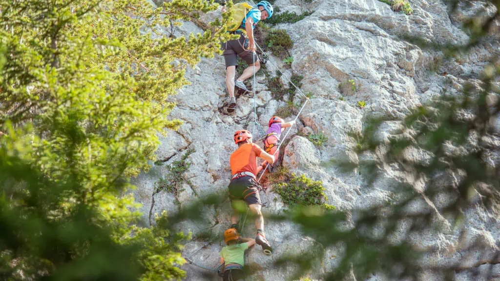 Eine Familie klettert gemeinsam an einem Klettersteig in den Bergen.